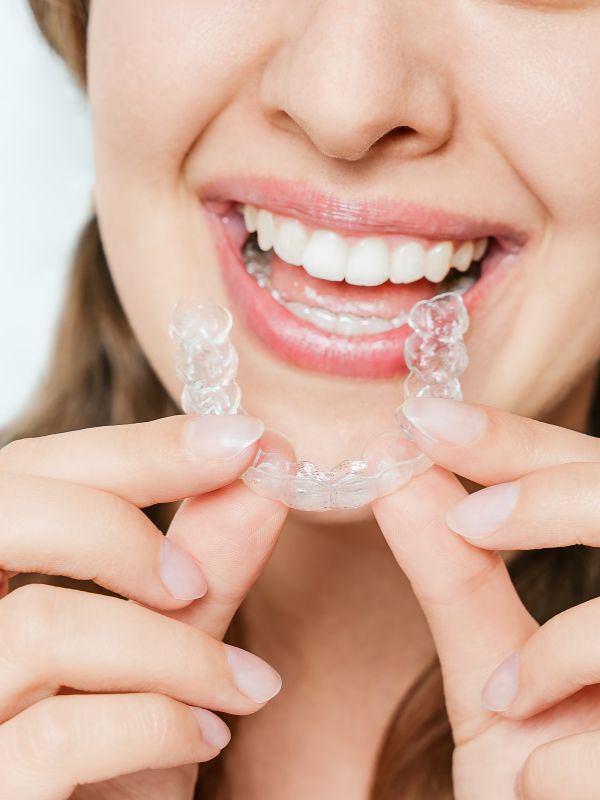 Woman holding a clear aligner tray for Invisalign treatment in Denver